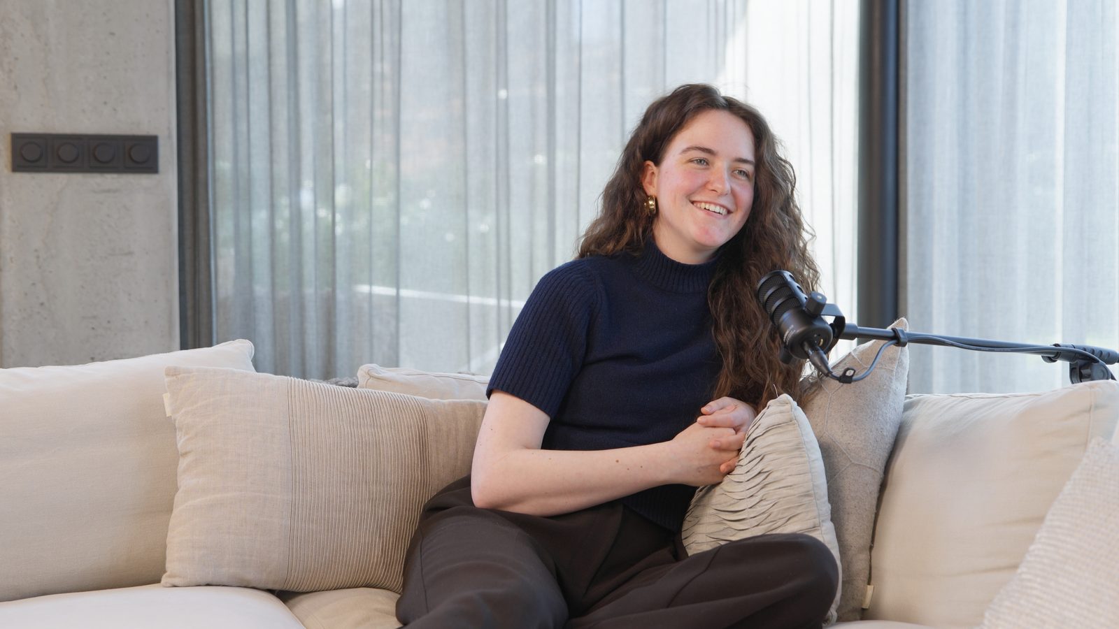 Podcastgast op een bank in het daglicht, achter een microfoon.