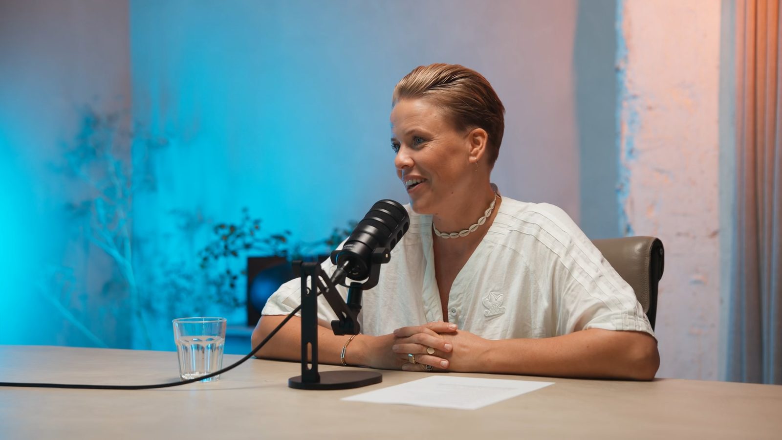 Podcastgast aan tafel, met blauw en warm licht op de muur achter haar.