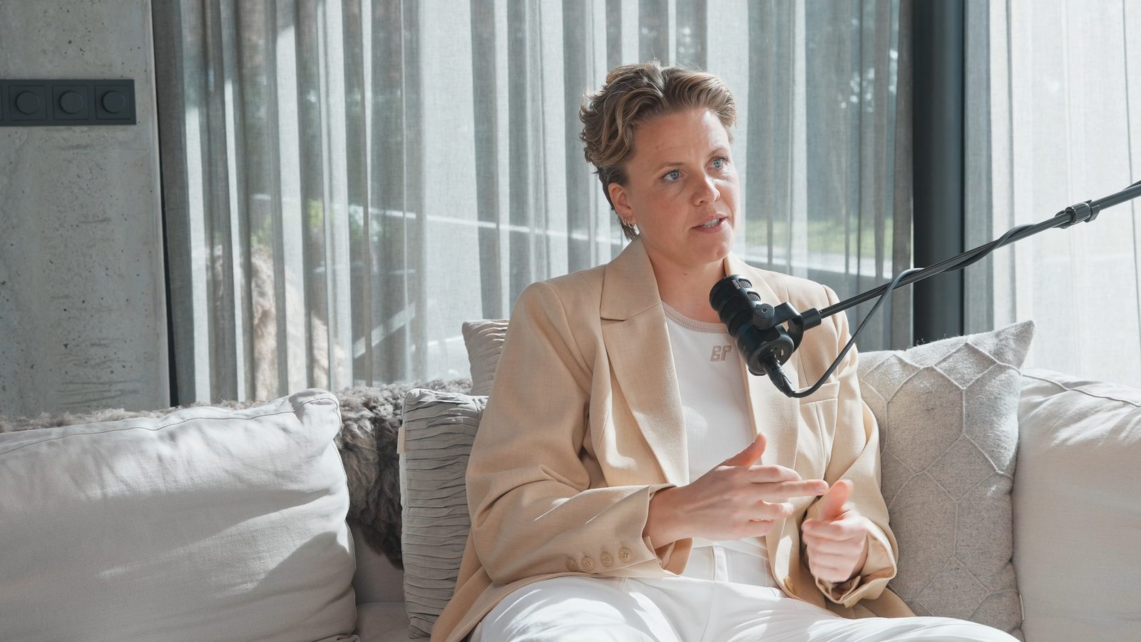 Podcastgast op een bank in een strak, modern interieur bij een groot raam.