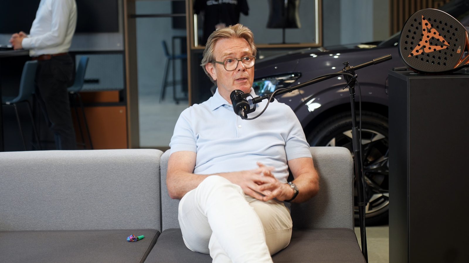 Podcastgast in gesprek op een bank in een autoshowroom, met een auto op de achtergrond.