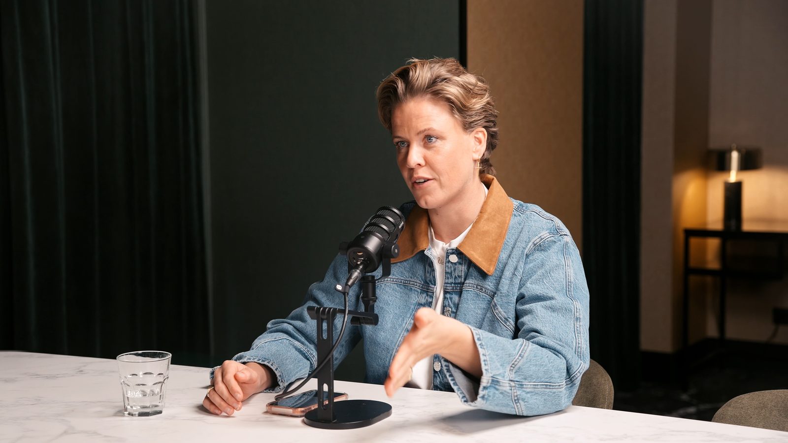 Podcastgast aan tafel achter een microfoon in een warm interieur met sfeerverlichting.